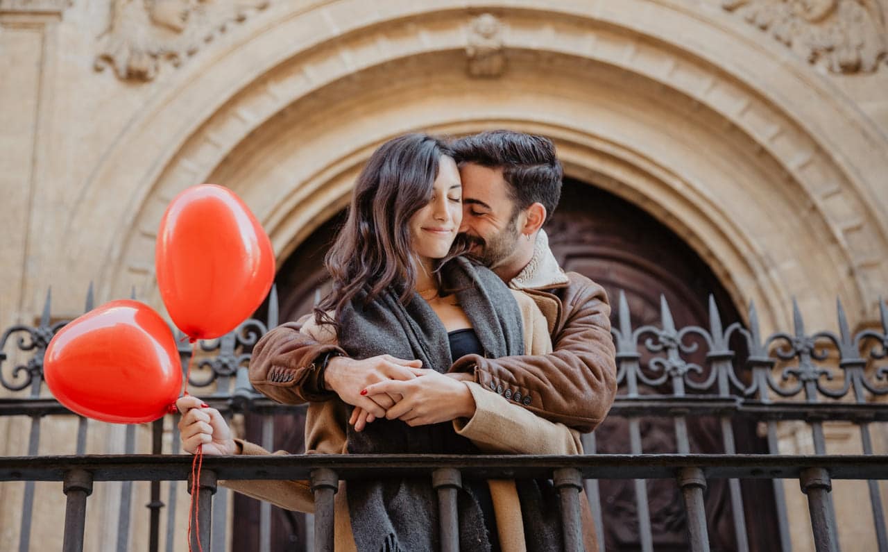 Couple embracing while holding red balloons
