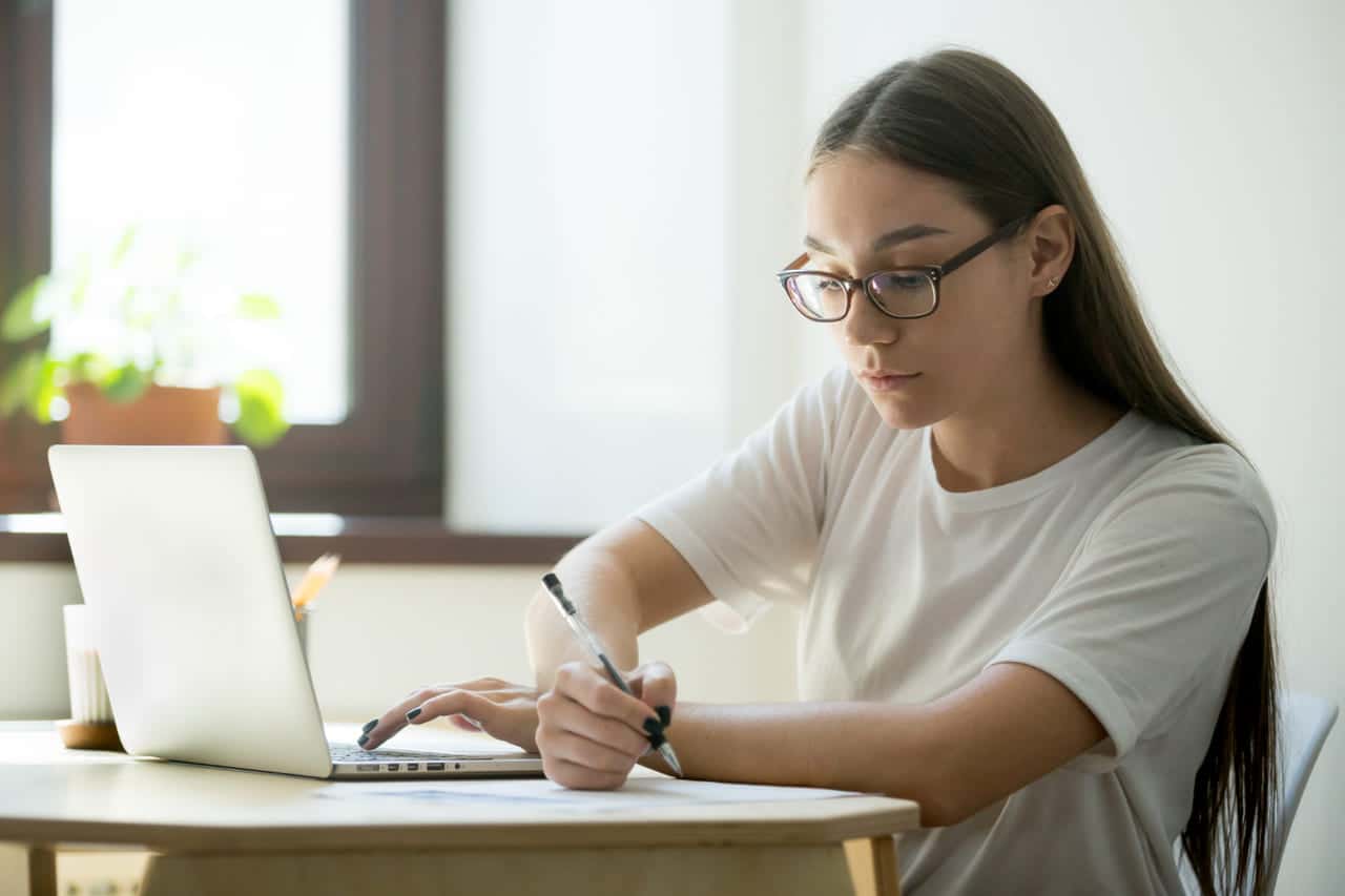 Woman writing notes while working on a laptop