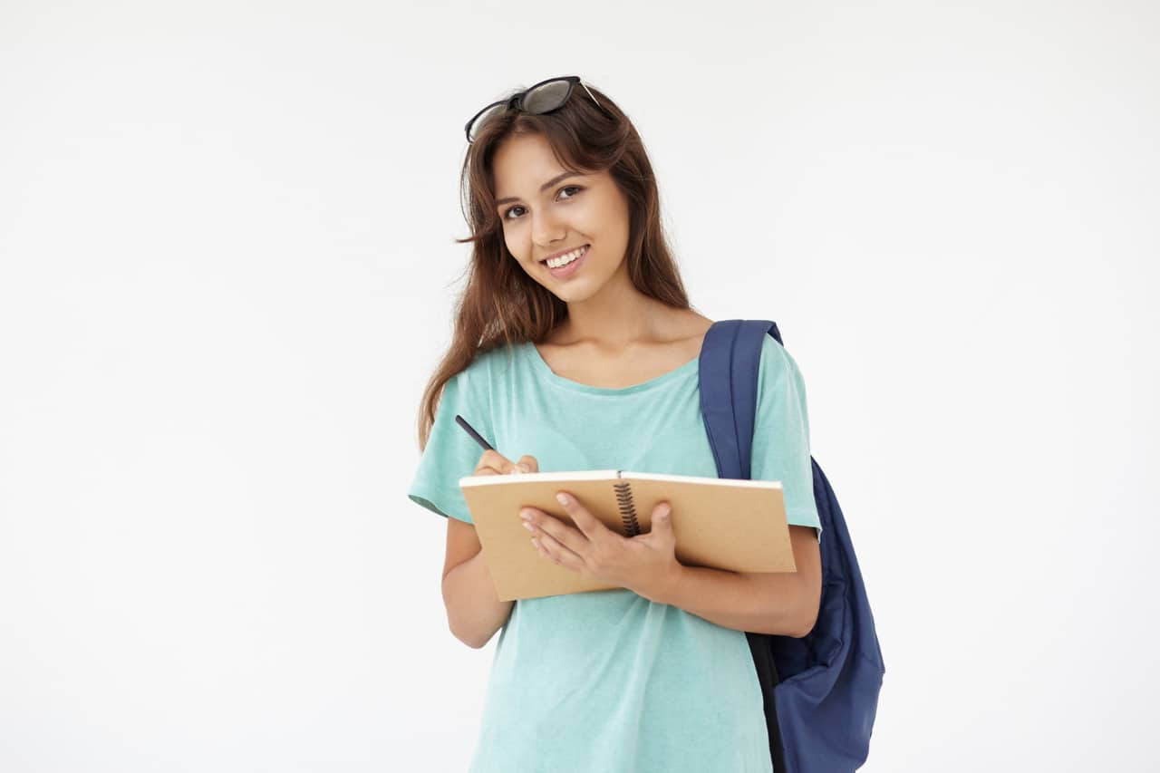Smiling student holding a notebook and pen with a backpack on