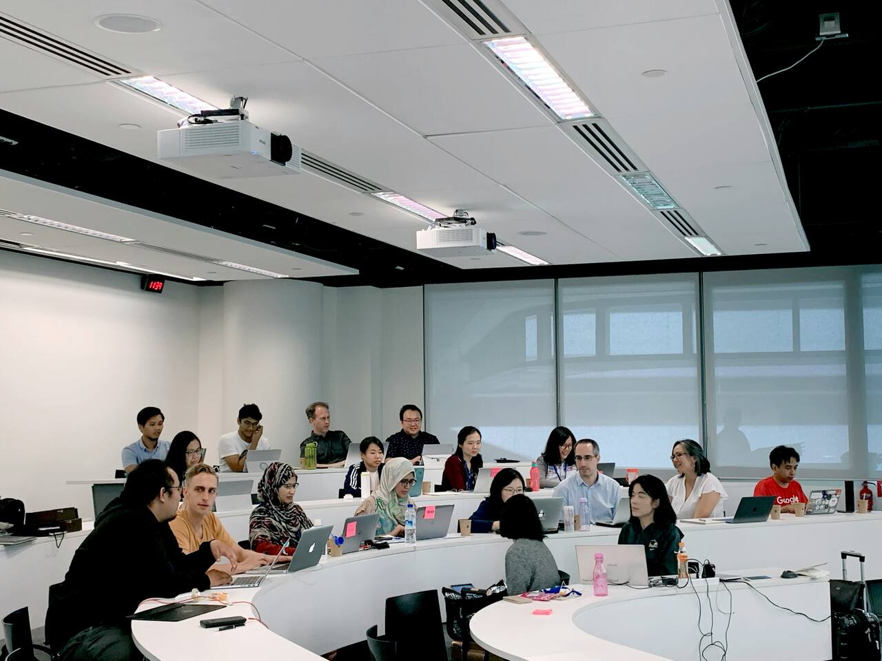 University students in a lecture hall, engaging in discussions and working on laptops during a class session.