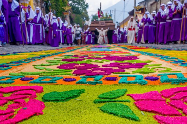 Colorful carpet during religious procession, participants in purple robes