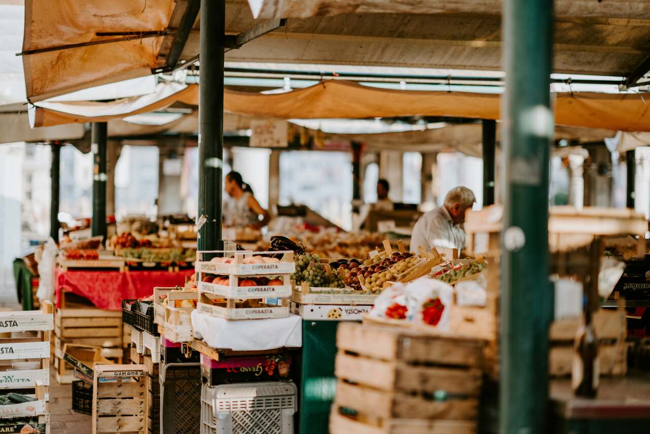 Open-air market with wooden crates filled with fruits and vegetables, and vendors setting up their stalls under a canopy