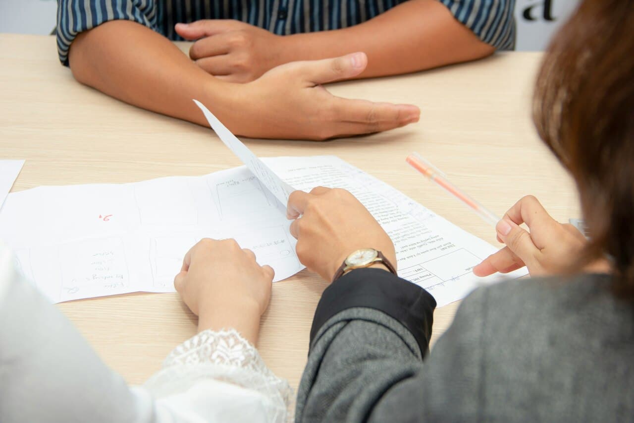 Professional business meeting between two women discussing documents at a desk with a laptop, promoting teamwork and collaboration in the workplace.